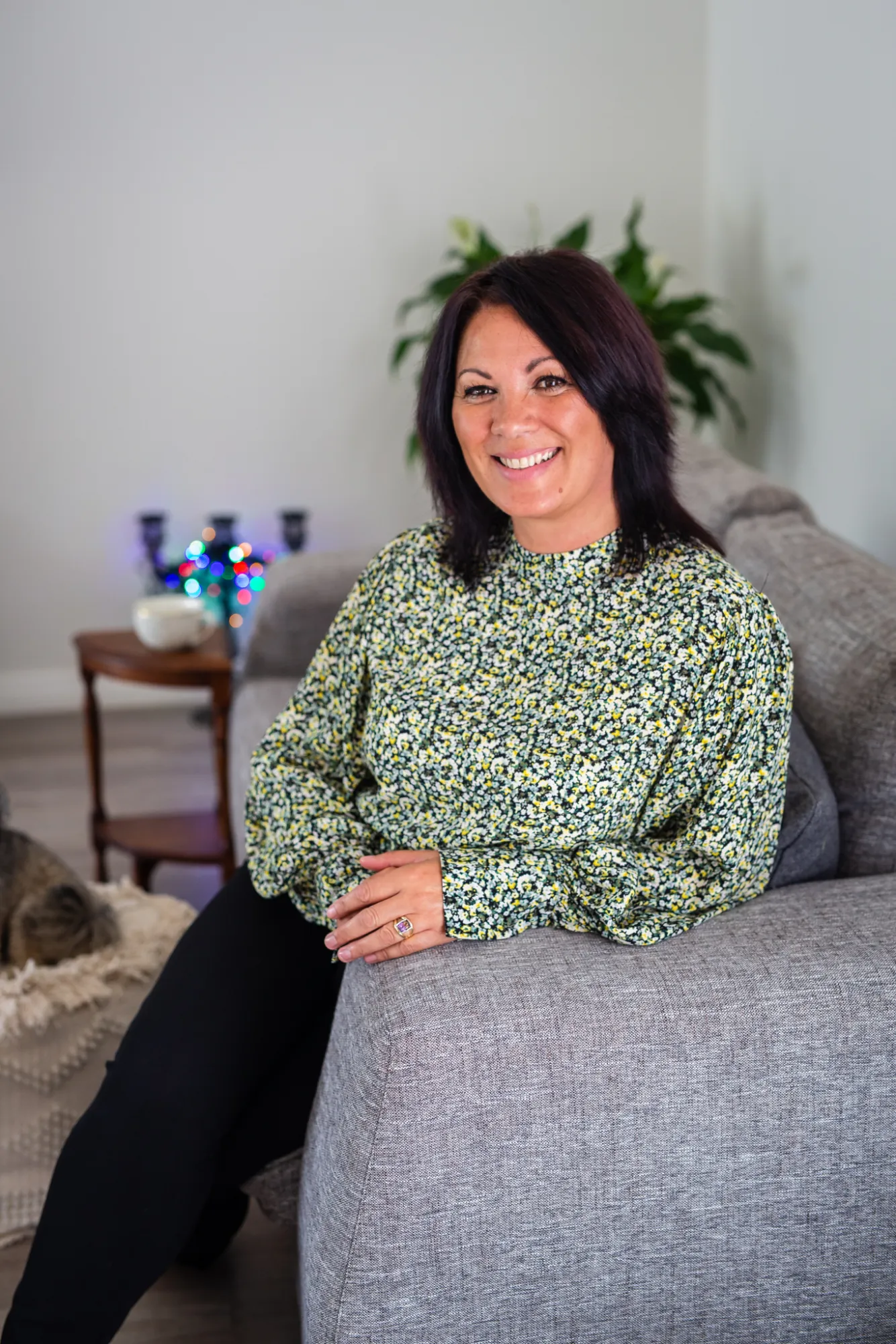 Sharon Gibson seated on a sofa in a green floral blouse, smiling warmly